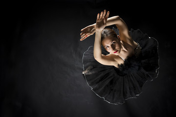 Beautiful expressive ballerina in the role of a black swan, wearing black tutu and pointe shoes on black background