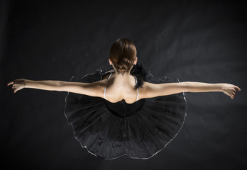 Back of beautiful ballerina in the role of a black swan, wearing black tutu and pointe shoes on black background