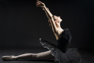 Beautiful ballerina in the role of a black swan, wearing black tutu and pointe shoes on black...