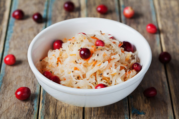 Sauerkraut or sour cabbage with cranberries in a white bowl on rustic wooden table, rural style