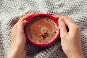 Womans hands holding a cup of hot cocoa or hot chocolate on knitted background, traditional...