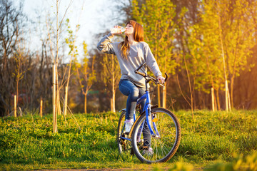 Fototapeta premium A young beautiful girl is drinking water from a bottle while sit