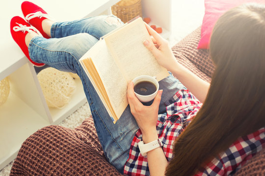Woman sitting on the sofa reading a book holding her coffee mug