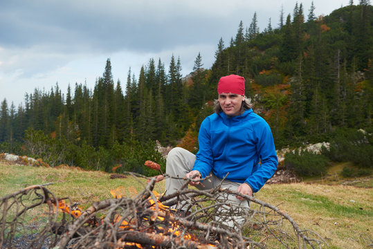 hiking man prepare tasty sausages on campfire