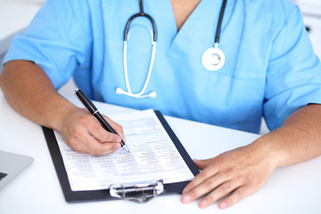 Portrait of unknown male surgeon doctor holding his stethoscope and filling up medical prescription