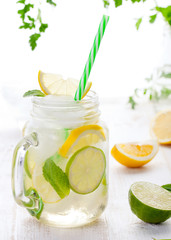 Lemonade with ice, lemon and lime slices in jar, straw.