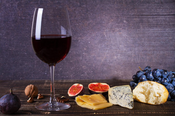Glass of red wine, cheese, grape, walnuts, figs, plums and apple on wooden background. Still life
