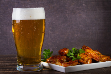 Glass of beer and chicken wings on dark wooden background