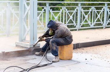 Worker in protective clothes cleans the metal structures sandbla