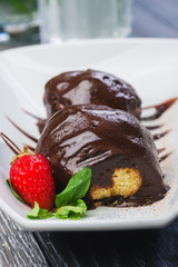 lush and beautiful chocolate truffle dessert with strawberries on a white plate on a wooden table in a restaurant