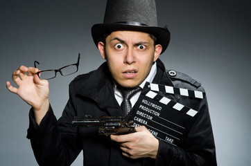 Young man with weapon and clapboard against gray