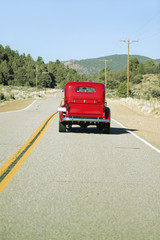 Fototapeta na wymiar A restored bright Red Roadster hotrod pickup truck, mid-30's, drives rural highway in Kern County near Lockwood Valley, CA