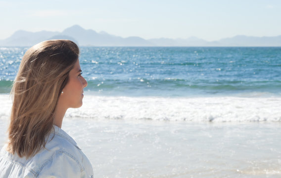 Frau mit blonden Haaren schaut auf das Meer