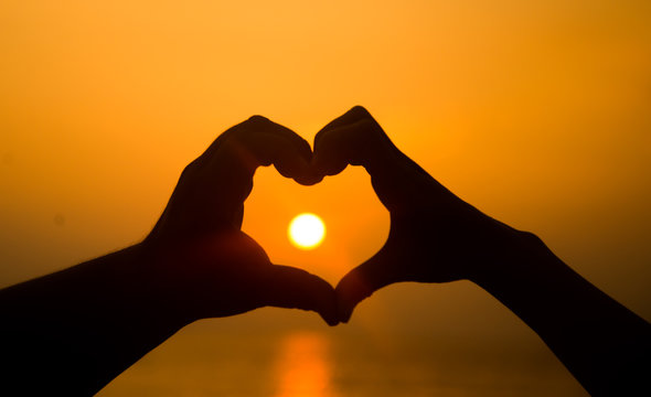 hand making heart shape over sunset