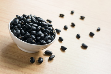 Fototapeta na wymiar Black beans in melamine cup white and scattered across wooden ba