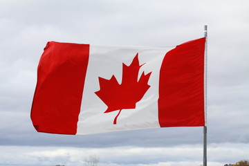 Flag of Canada gently waving in a light breeze against clouds and blue sky. 