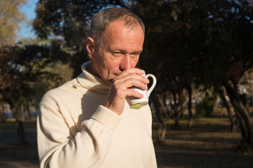 Attractive man deep in thought, drinking coffee, standing  in th