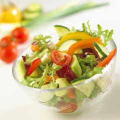 Bowl of fresh mixed salad with ingredients behind.
