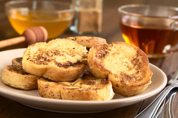 French toast made of baguette, honey, cinnamon powder and cup of tea in the back, photographed with natural light (Selective Focus, Focus on the front edge of the upper toasts)