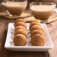Homemade rum balls covered with cocoa powder, glass cups of hot chocolate in the back, photographed with natural light (Selective Focus, Focus on the two balls in the front)