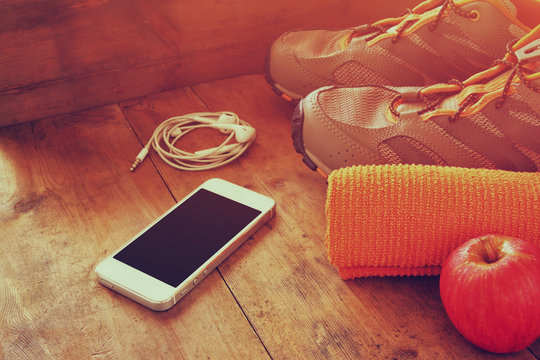 fitness concept with mobile phone with earphones, towel, apple and sport footwear over wooden background. retro filtered
