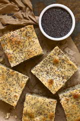 Poppy seed cake pieces on paper with poppy seeds on the side, photographed overhead on slate with natural light