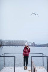 girl in a hat and jacket standing on the dock at the lake in winter