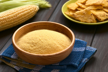 Wooden bowl of cornmeal with homemade tortilla chips and cobs of corn in the back, photographed on dark wood with natural light (Selective Focus, Focus one third into the cornmeal) - obrazy, fototapety, plakaty