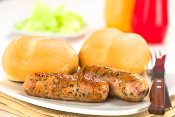 Fried bratwurst with bun, traditional German fast food served on plate with ketchup, mustard and green salad in the back (Selective Focus, Focus on the front of the first bratwurst)