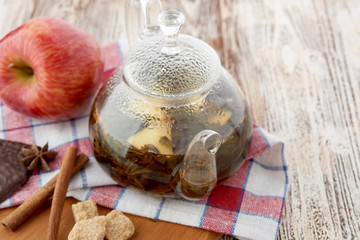 Ripe apple, cinnamon and fruit drink in glass teapot on wooden background