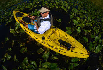 man kayak fishing in lily pads