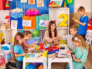 Kids holding colored paper and glue on table in kindergarten .