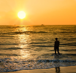Silhouette of the young man coming into sea waves under sunset light.