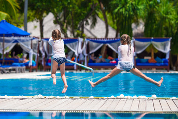 Fototapeta na wymiar Adorable little girls having fun in outdoor swimming pool on summer vacation