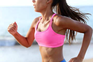 Midsection of determined woman jogging on beach. Young female is wearing sports bra and shorts....
