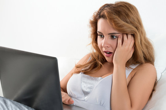 Young shocked woman reading something at laptop