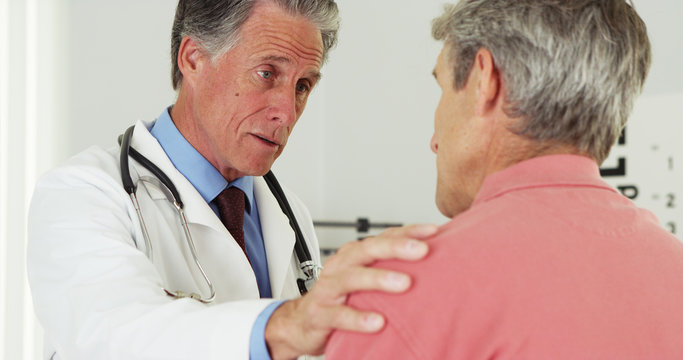 Senior doctor talking to elderly patient with hand on shoulder