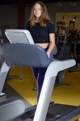 Attractive young woman smiling and doing cardio exercise on treadmill at gym