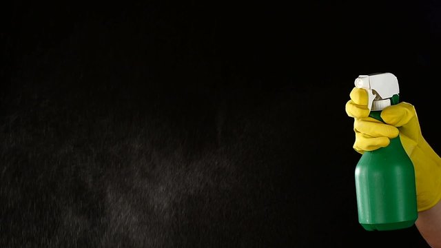 Hand in glove holds spray bottle, on black, slow motion