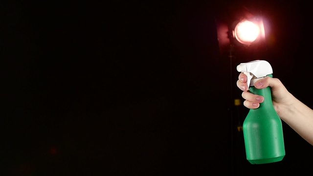 Hand holds spray bottle, on black, slow motion, back light