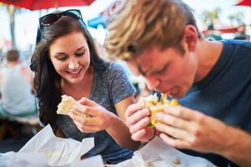 couple eating hamburgers together at outdoor restaurant patio during summer