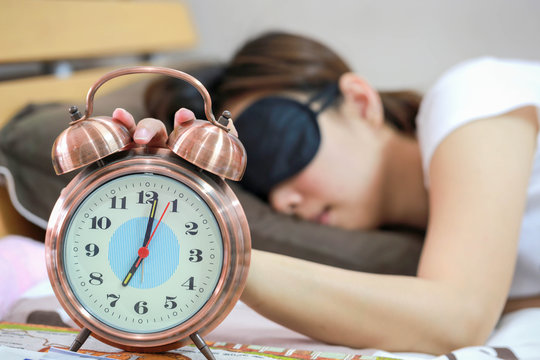 Young women sleepy in bed with blindfold and closed clock.