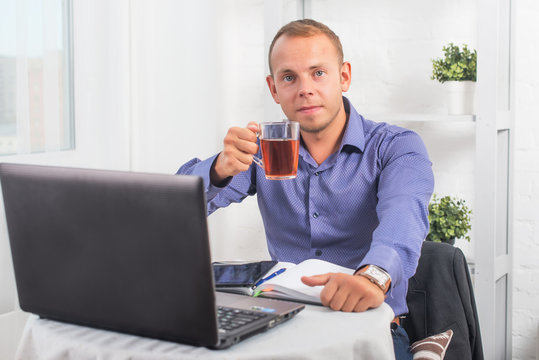 Businessman working in office, sitting at  table holding a cup and looking straight
