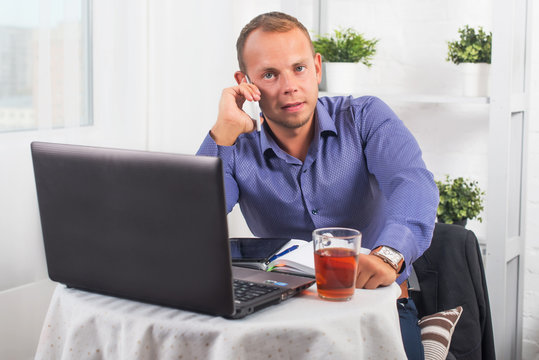 Young businessman working in office, sitting at a table, looking straight and talking on the phone