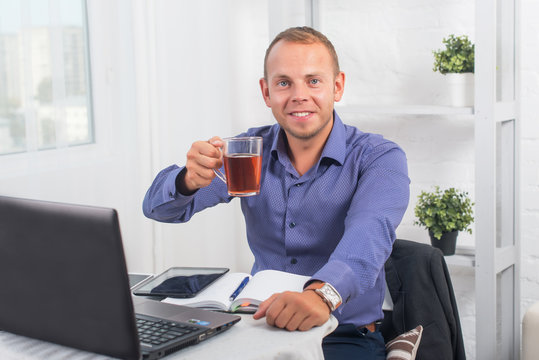 Businessman working in office, sitting at a table holding cup and looking straight.