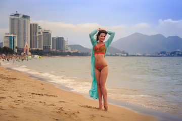 brunette girl in bikini transparent frock stands tip-toe on sand