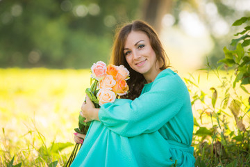 Naklejka premium Portrait of a young girl with a bouquet of roses sitting in the shade of the trees on a sunny day