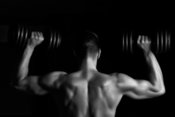 Handsome young muscular man lifting weights over dark background