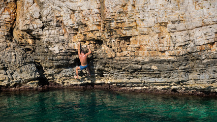 Young athletic man climbing sea cliffs without rope or harness in Croatia
