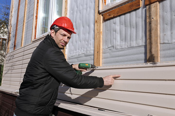 A worker installs panels beige siding on the facade